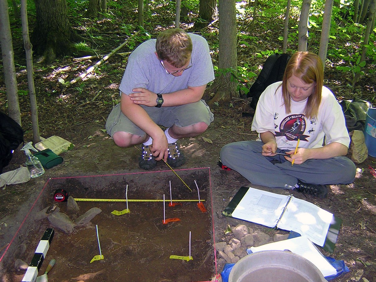 Deux étudiants en stage de pratique de terrain relèvent l’emplacement des faits archéologiques.