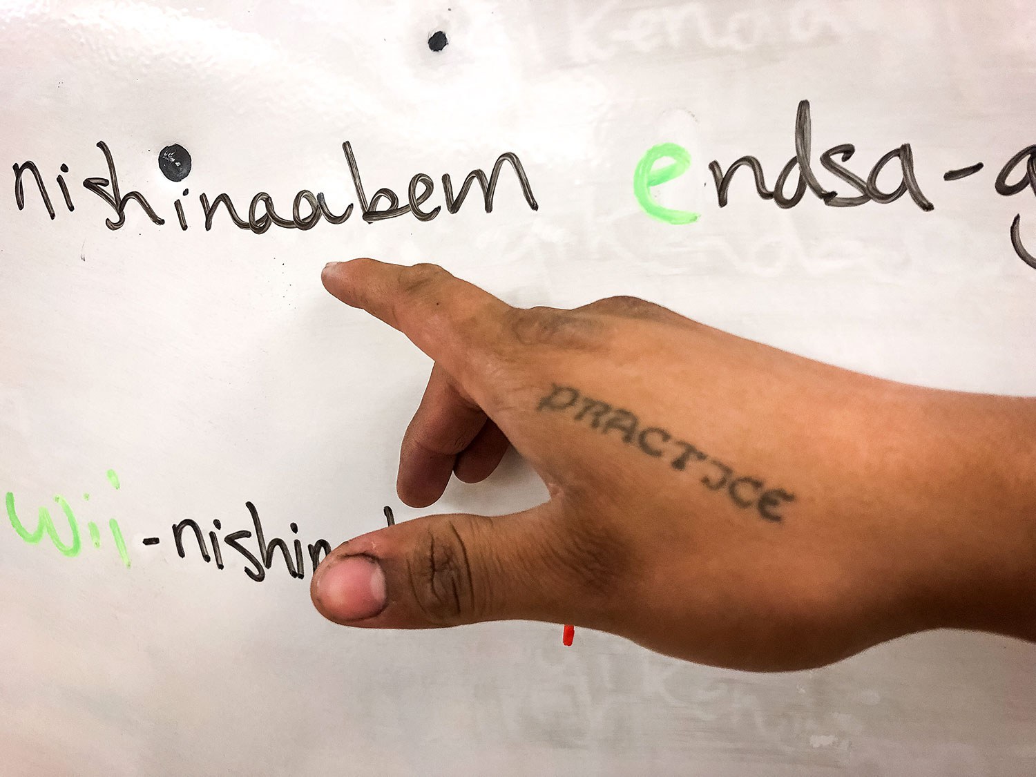 Un tatouage sur la main du professeur Ninaatig Pangowish tient lieu d’appel permanent à la pratique (« pratice ») de la langue.